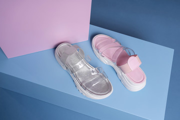Fashionable gray and pink open slippers with a white sole stand on a pink, blue stand from the studio. Promotional photo