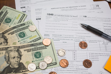 Blank IRS Tax return1040 for 2019 surrounded by US0 20 dollar bills and coins on a wooden table with black pen. Individual Income Tax Return. The time to pay taxes