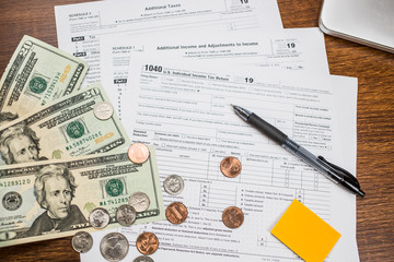 Fototapeta na wymiar Blank IRS Tax return1040 for 2019 surrounded by US0 20 dollar bills and coins on a wooden table with black pen. Individual Income Tax Return. The time to pay taxes