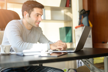 A young man working at a desk with a laptop. Calculator, notepad, pencil, pen and cup of coffee on the side.