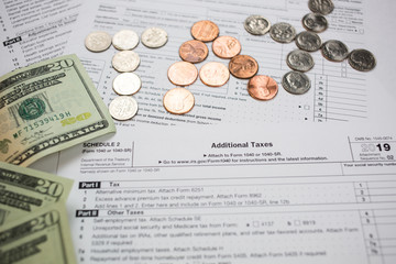 tax word made of US coins forming letters on a blank IRS Tax return form 1040 for 2019 along with 20 dollar bills. Tax season