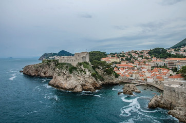 Fototapeta na wymiar View of city walls of Dubrovnik and blue sea, Dubrovnik, Croatia. Dubrovnik old town surrounded by old walls. View from above of red rooftops, roofs and fortress.