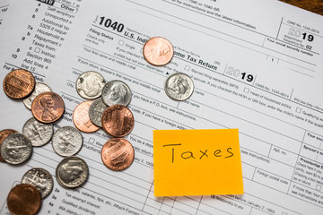 Word Taxes, text on sticker with blank 1040 tax return U.S. IRS form and coins on top. Tax season.