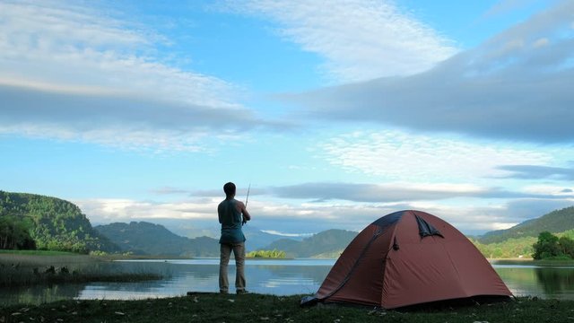 Man stands near the hiking tent and casting the lure and fishing from the coast. Fishing in Chilean Patagonia