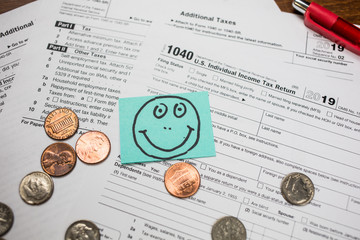 IRS 1040 tax return form with smiley face drawn on a sticker. Wage and tax statement concept