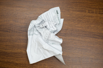USA IRS tax form 1040 crumpled on a wooden table. Concept for frustration, difficulty and needing help in understanding tax laws and regulations