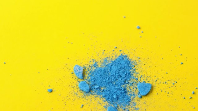 Close-up shot of crushed blue eyeshadow falling down on table with bright yellow surface