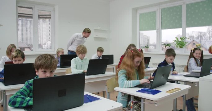 Education in the modern school, children use laptops, teacher monitors the implementation of the test work, the learning process at school.