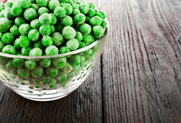 Transparent glass bowl with frozen pea on a old wooden table.