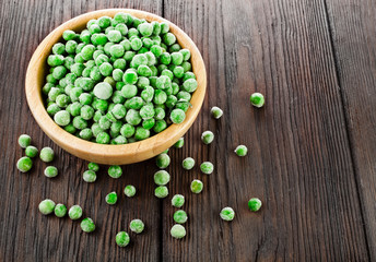 Bowl of frozen pea on a old wooden table.