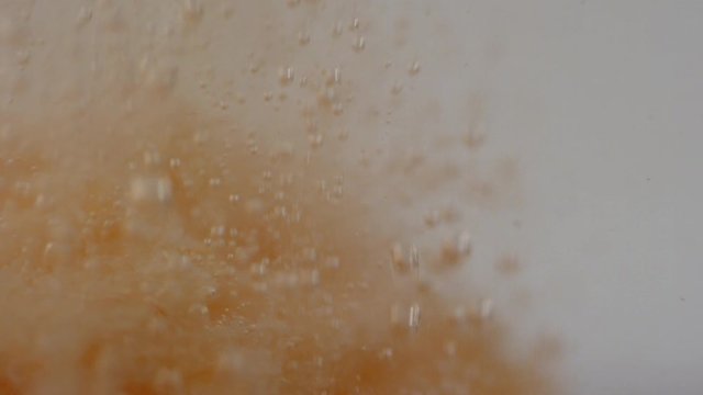 Underwater macro tracking shot of peachy bath bomb exploding and creating small bubbles in water in slow motion