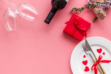 Romantic dinner on Valentines Day. Wine, plate, present box on pink background top-down copy space