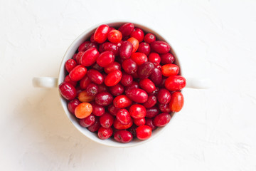 Dogwood is a sweet and sour red fruit. medicinal plant. ripe vitamin berries. Dogwood on a wooden white background in a white plate with space for text. The concept of a healthy lifestyle. gardening