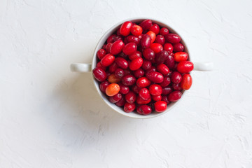 Dogwood is a sweet and sour red fruit. medicinal plant. ripe vitamin berries. Dogwood on a wooden white background in a white plate with space for text. The concept of a healthy lifestyle. gardening