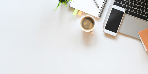 Top view image of accessories on the white table as background. Laptop, Black blank screen smartphone, notes, potted plant and pencil putting together as flat lay.