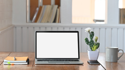 Photo of white blank screen laptop putting on the wooden working desk including cactus, coffee cup, notebook and smartphone. Modern working desk concept.