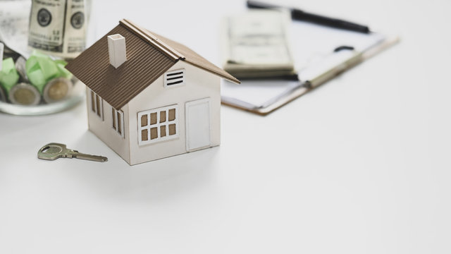 Close-up image of House model, saving money, key, agreement on clipboard and money putting together on white table. Concept of saving plan for purchase a property.