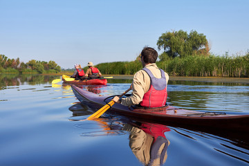 Rear view of man paddling the wooden kayak and couple in red kayak kayaking in the lake or river