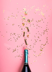 Green champagne bottle with golden streamers flow as bubbles on pink monochrome color background. Celebrating new year, christmas, valentine's day festive flat lay. Anniversary, birthday party concept