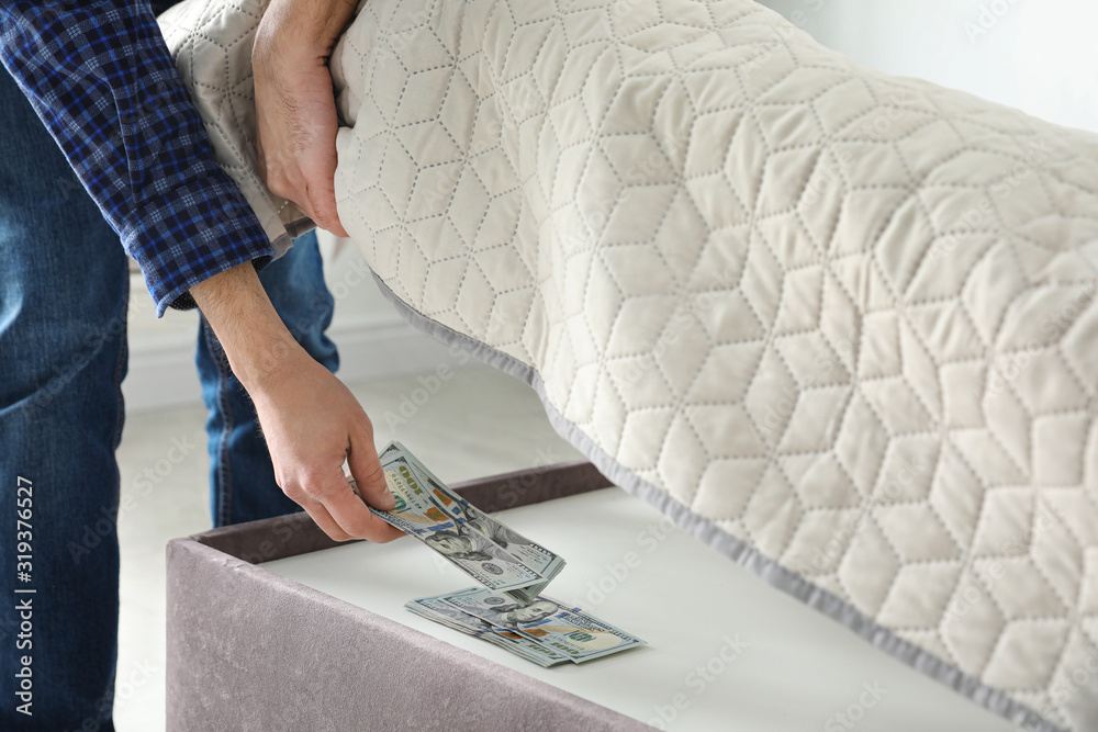 Wall mural Man hiding dollar banknotes under mattress in bedroom, closeup. Money savings