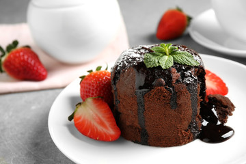 Delicious warm chocolate lava cake with mint and strawberries on table, closeup