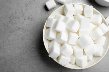 Refined sugar cubes in bowl on grey table, top view
