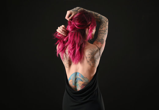 Beautiful woman with tattoos on body against black background, back view