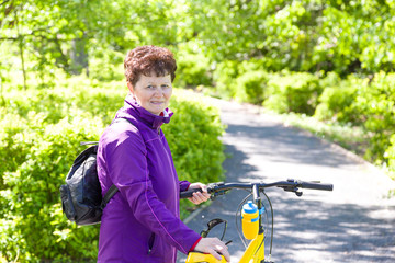 Portrait of happy adorable mature woman riding a bike in summer park