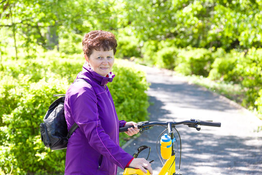 Portrait Of Happy Adorable Mature Woman Riding A Bike In Summer Park