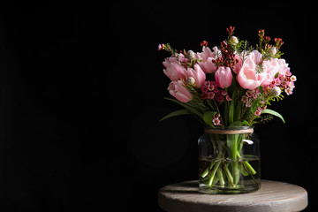 Naklejka na ściany i meble Beautiful bouquet with spring pink tulips on wooden table against black background. Space for text