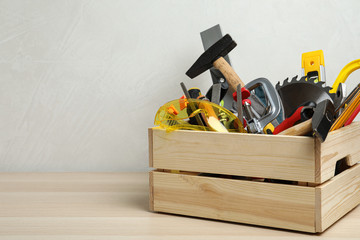 Crate with different carpenter's tools on wooden table. Space for text
