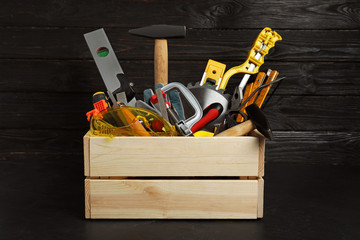 Wooden crate with different carpenter's tools on black table