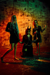 Women in halloween outfit posing with red fire background. Gorgeous girl in clothes celebrates the day of the dead. Halloween concept, witch costume, bright colors, red and green filters