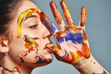 Portrait of a beautiful girl in the paint. Closeup portrait of a girl with face and hands with different paint. Fashion art concept, beauty, creative people freelance people