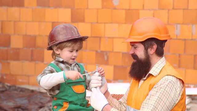 Little son worker erecting a brick wall. Boy play as builder or repairer. Son helper. Child dreaming about future career in architecture or building. Happy family building a house.