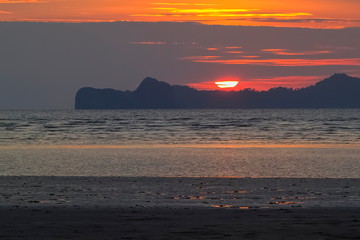 view panorama seaside evening of sand beach with mountain and red sun light in cloudy sky background, sunset at Chao Mai Beach, Had Chao Mai National Park, Trang Province, southern of Thailand.