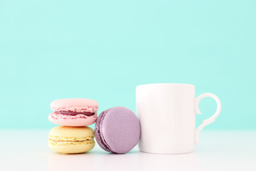 White cup of coffee and colorful macaron or macaroon over pastel wooden table