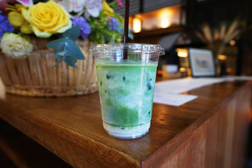 Close up plastic take away cup of Iced Matcha green tea with milk on wooden table