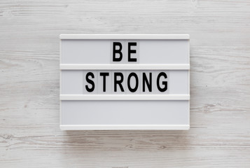 'Be strong' words on a lightbox on a white wooden background, top view. Overhead, from above, flat lay.