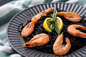 close up black pasta with cuttlefish ink with king prawns and lemon wedges in grey plate on kitchen towel