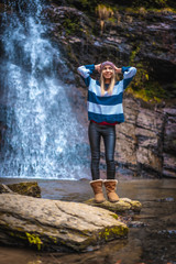 Obraz premium A straight-haired blonde in a blue and white wool sweater with her hands on her head in a waterfall. Lifestyle session
