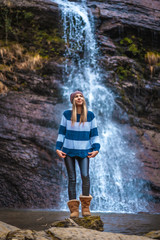 A straight-haired blonde in a blue and white wool sweater looking up at a waterfall. Lifestyle session