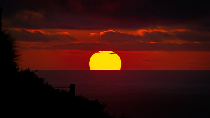 Fototapeta na wymiar View of orange sun setting into Tasman sea with dark clouds