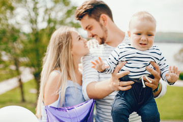 A young and beautiful blonde mother in a blue dress, along with her handsome man dressed in a white jacket, playing with her little son in the summer solar park