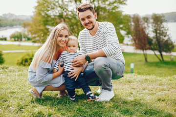 A young and beautiful blonde mother in a blue dress, along with her handsome man dressed in a white...