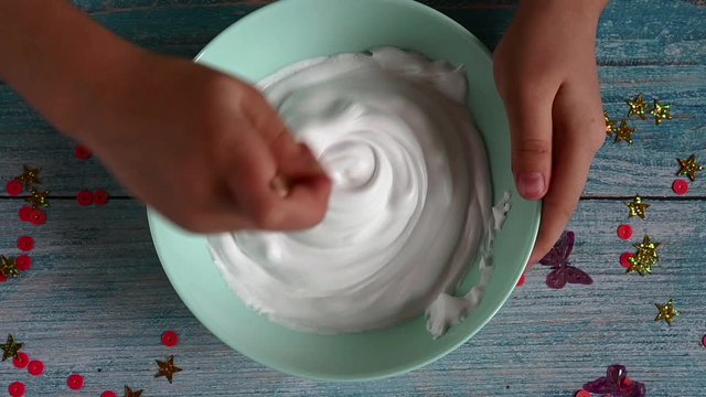 a little girl hands making slime herself on blue wooden background. the child is mixing the slime mix