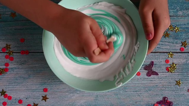 a little girl hands making slime herself on blue wooden background. the child is mixing the slime mix and blue paint