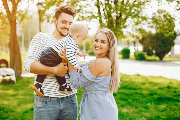 Fototapeta premium A young and beautiful blonde mother in a blue dress, along with her handsome man dressed in a white jacket, walks with her little son in the summer solar park