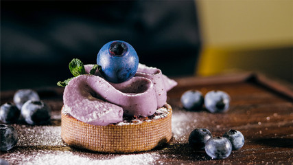 Cake with purple cream and powdered sugar on the table near the blueberries, close-up.