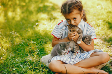 beautiful and cute girl in blue dresses with beautiful hairstyles and make-up sitting in a sunny green garden and playing with a cats